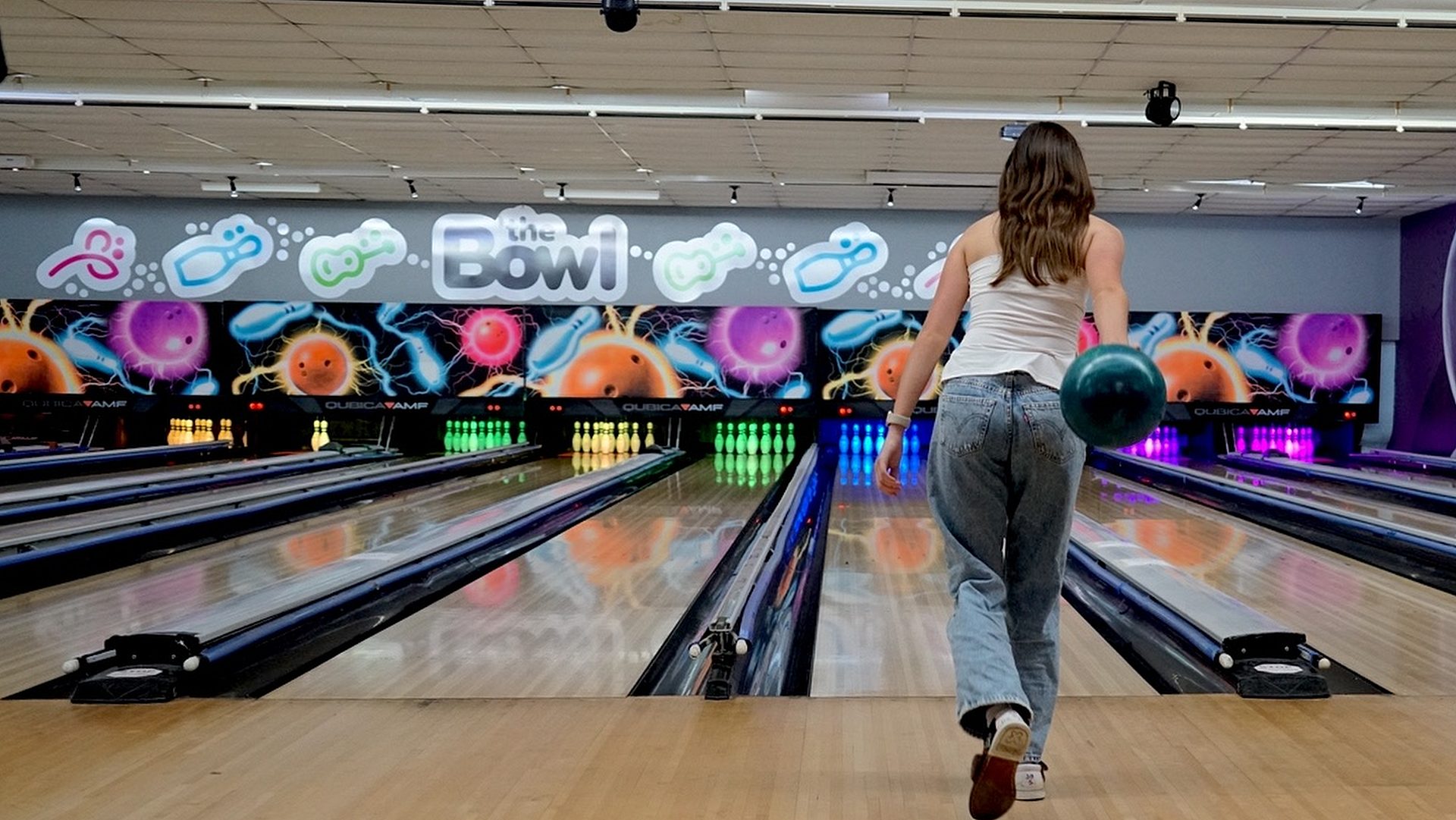 A girl in a white top and jeans about to roll a bowling ball down the glowing lanes at The Bowl in Port Macquarie