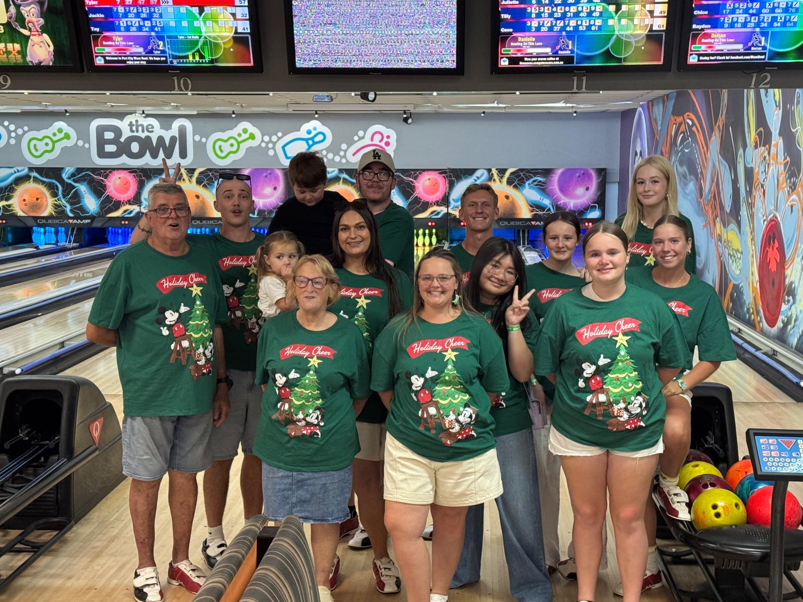 A work team in matching green Holiday Cheer Christmas t-shirts posing together at the bowling lanes at The Bowl