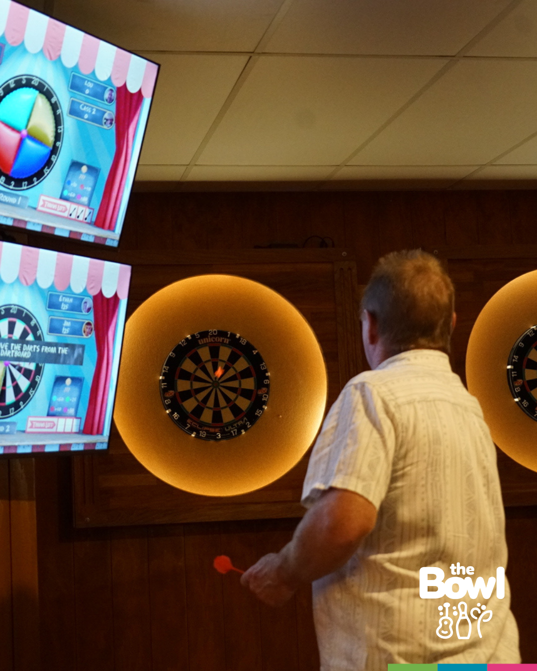 A player throwing at a lit electronic dart board with scoring screens at The Bowl in Port Macquarie