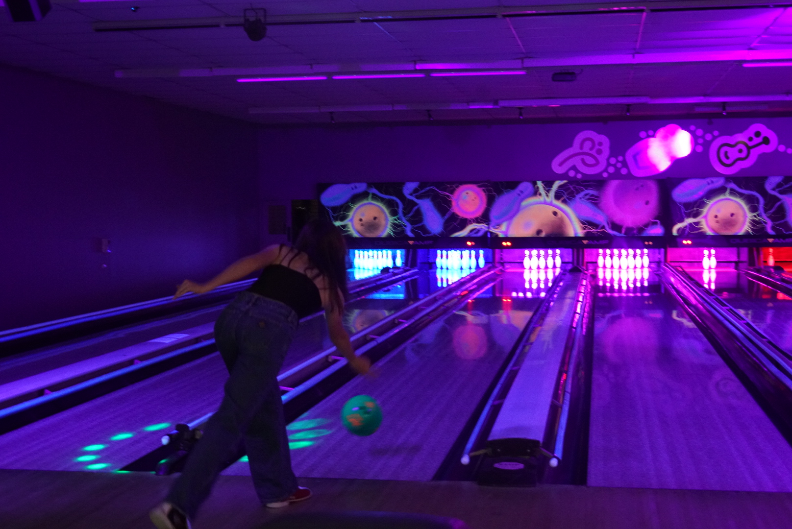 A bowler rolling a ball down the glowing UV lanes at The Bowl in Port Macquarie, with colourful mural art above the pins