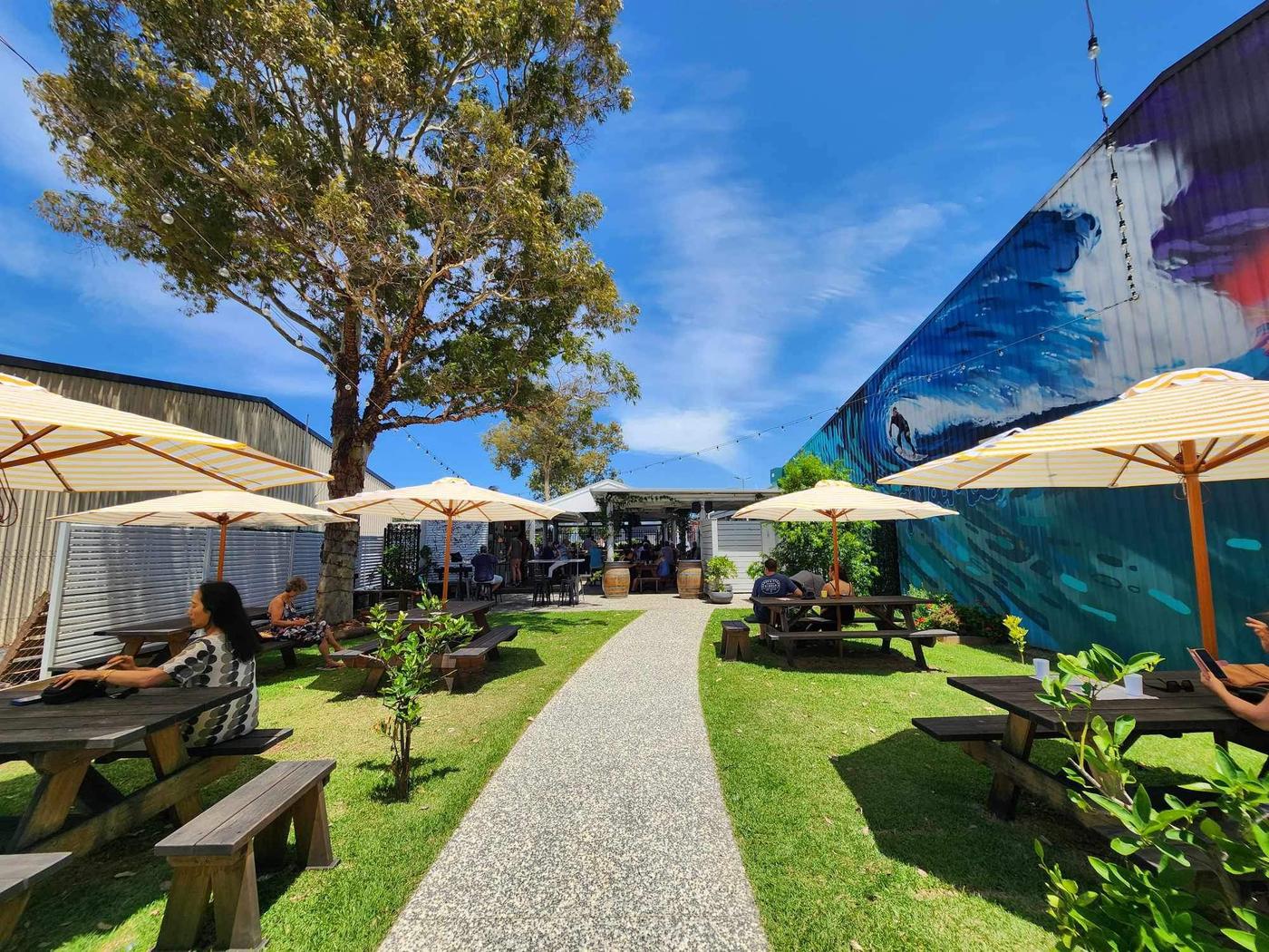 The Terrace at The Bowl Port Macquarie by day, with yellow umbrellas, picnic tables and lawn under a blue sky