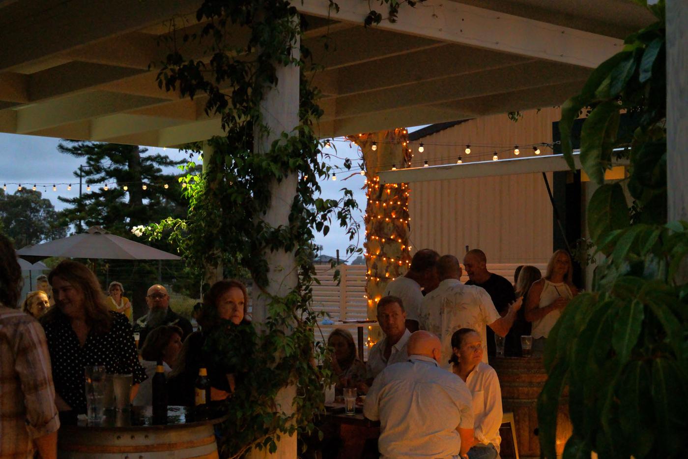 Friends enjoying drinks at the barrel bar under string lights on The Terrace at The Bowl Port Macquarie in the evening